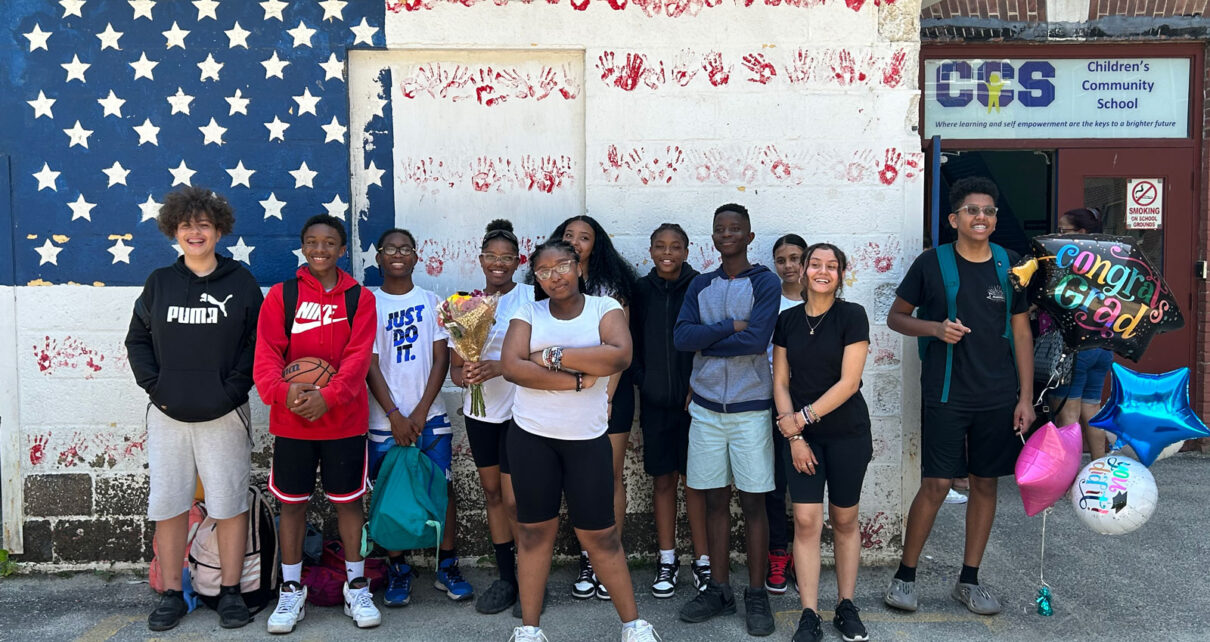 Students standing in front of American flag mural where red stripes are hand prints